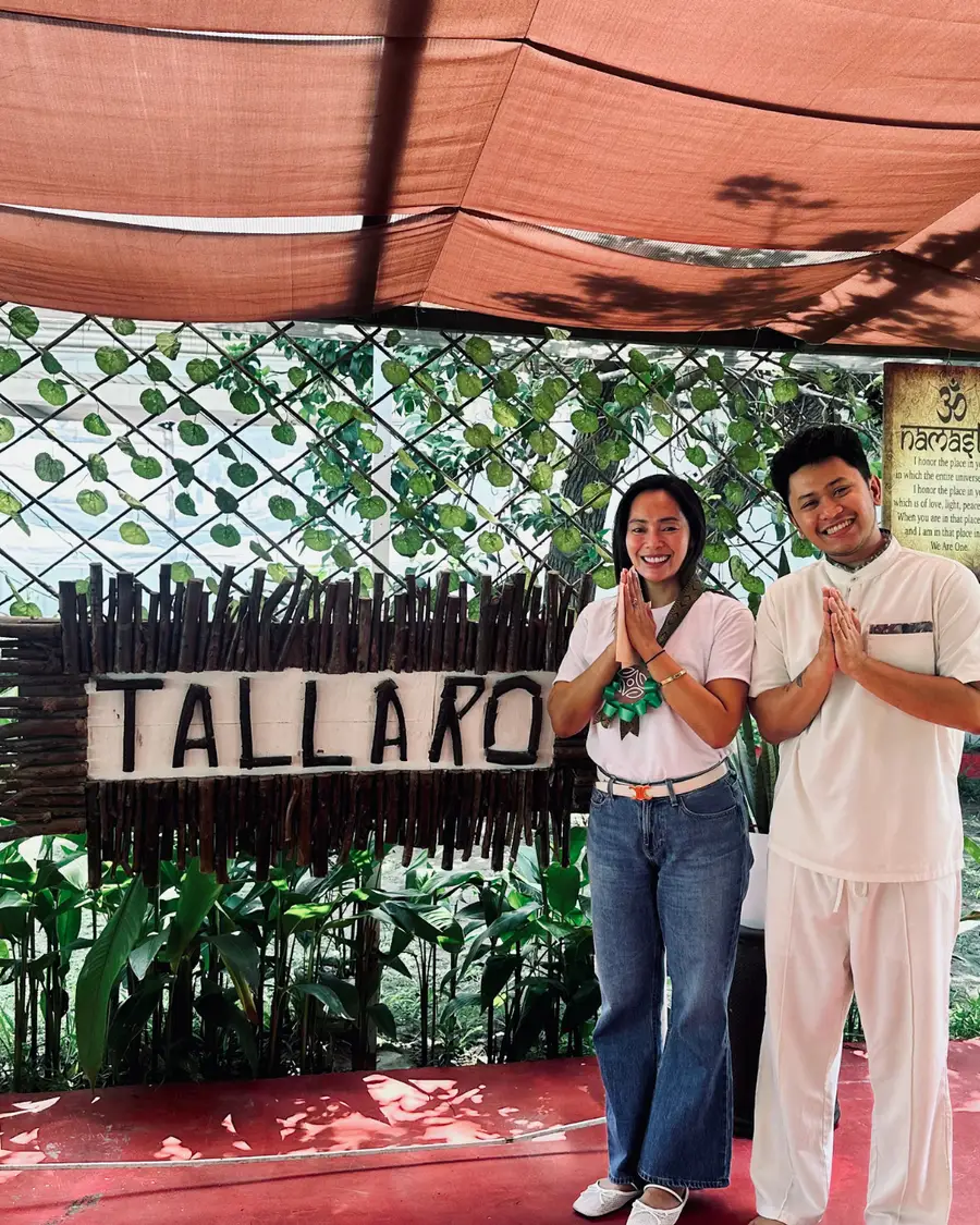 Dr. Femilyn S. Domingo greeting a Tallaro facilitator with hands pressed together beside the Tallaro sign in the healing centre garden.